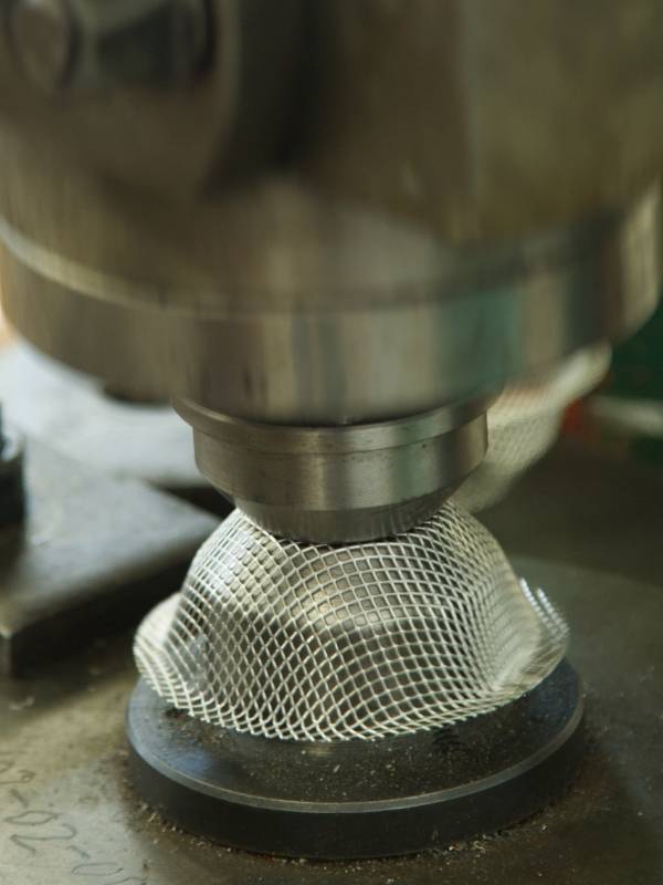 The machine is pressing the wire mesh into conical shapes.
